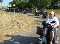 Getooid met de gele vierdaagse petjes toeren de berijders van scootmobielen door de bocht.